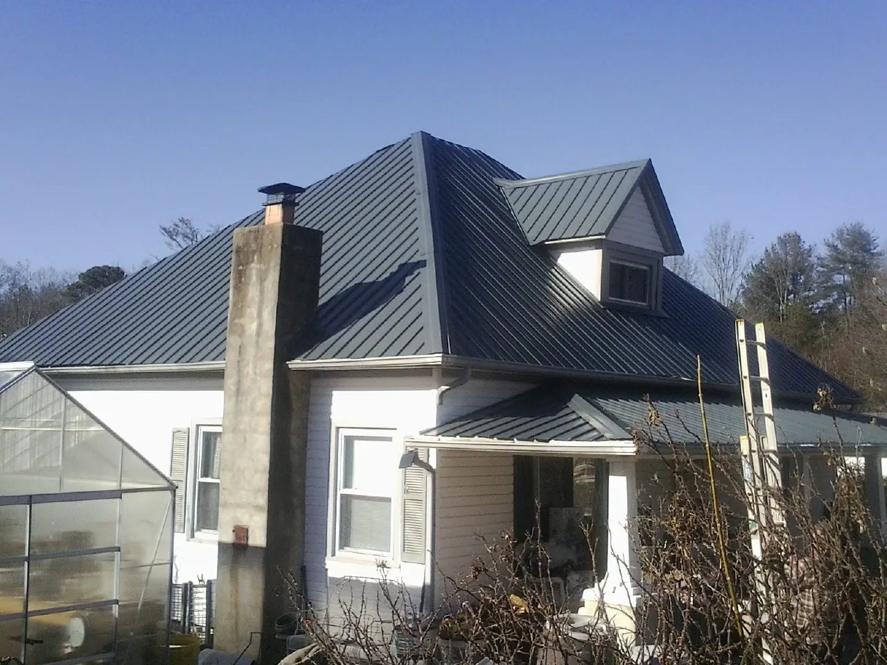 Dark blue standing seam metal roof on a white farmhouse with dormer — Slate & Tile Roof Repair by Roofing Brothers in Sheboygan Falls