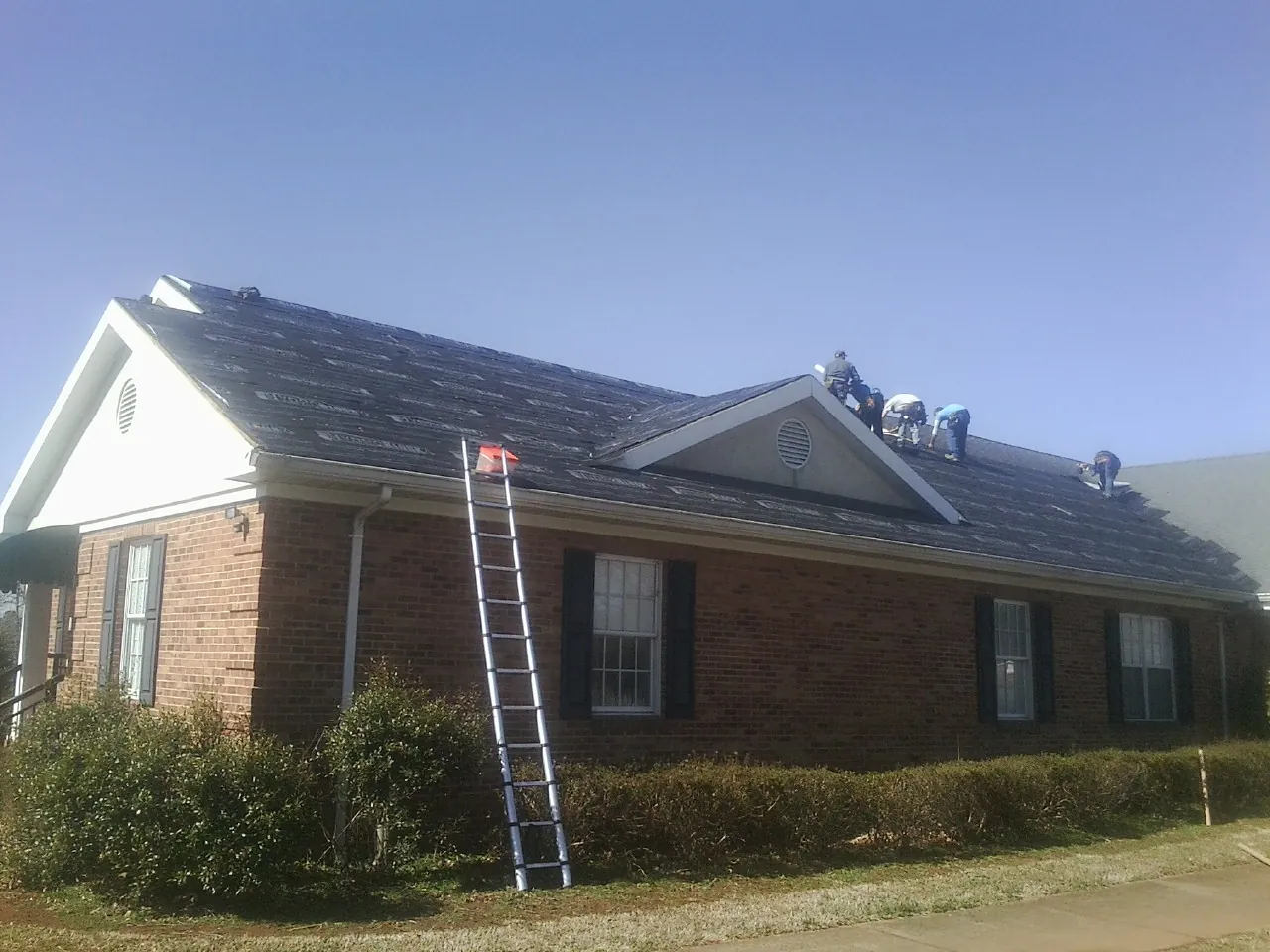 Crew tearing shingles off a brick ranch roof with a ladder set — Emergency Roof Repair work by our crew in Sheboygan Falls