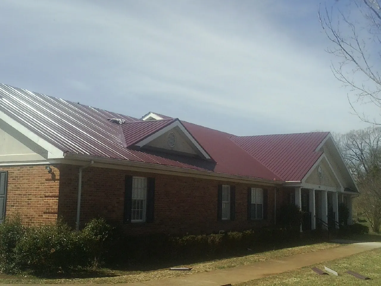 Red metal roof with gabled entries on a long brick building, from a Hail Damage Roof Repair job in Sheboygan Falls