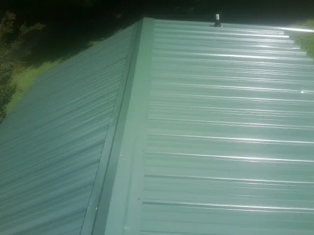 New green metal panels meeting at the ridge of a roof — Flat Roof Repair work by our crew in Sheboygan Falls