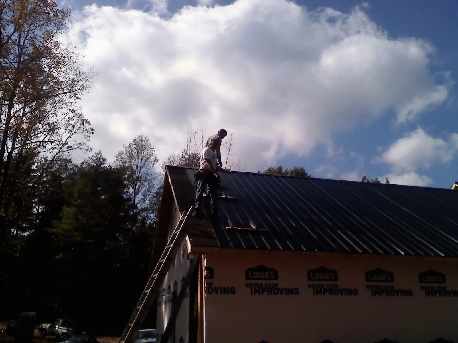 Roofer fastening dark metal panels high against a cloudy sky in Sheboygan Falls