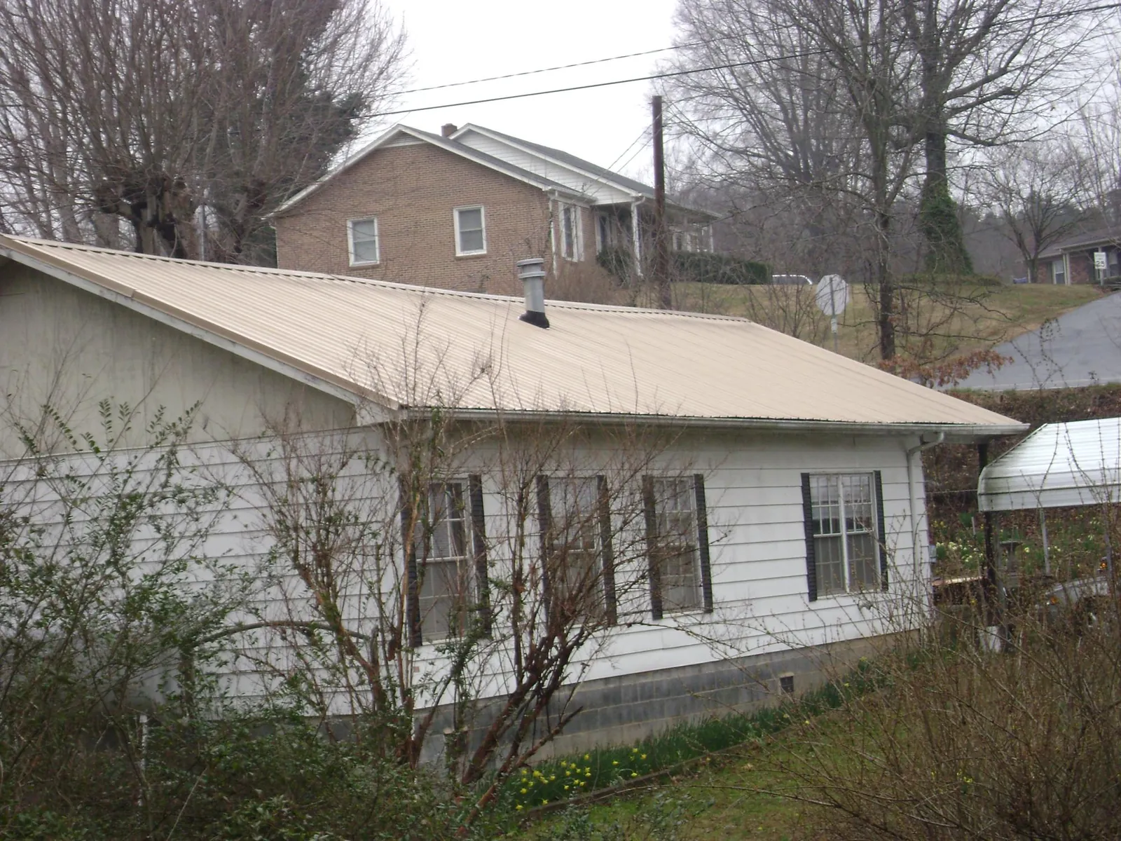Tan metal roof on a white sided house set into a hillside — Commercial Roofing by Roofing Brothers in Sheboygan Falls