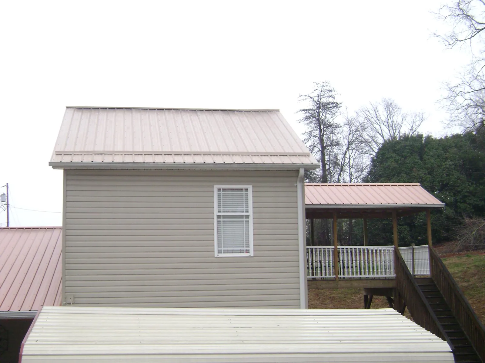 Tan metal roofs on a two story addition and attached porch, from a Roof Replacement job in Sheboygan Falls