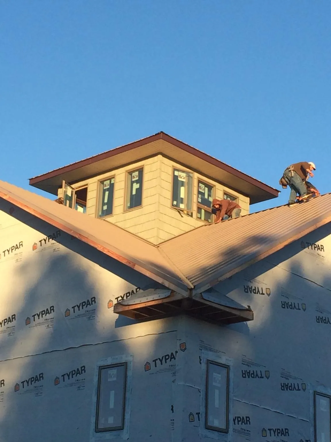 Roofers working around a rooftop cupola on a new metal roof at sunset — Roof Waterproofing in Sheboygan Falls by Roofing Brothers
